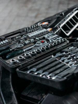 Tool case with wrenches and metal nuts lying on opened car hood in workshop