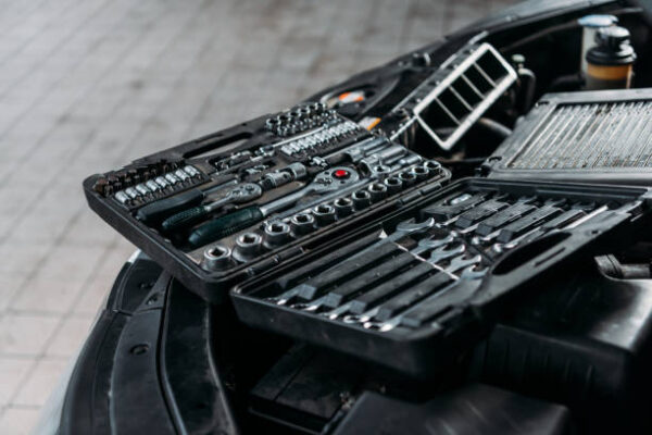 Tool case with wrenches and metal nuts lying on opened car hood in workshop