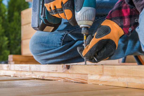 Male carpenter using cordless drill to drive long screw through wooden planks.